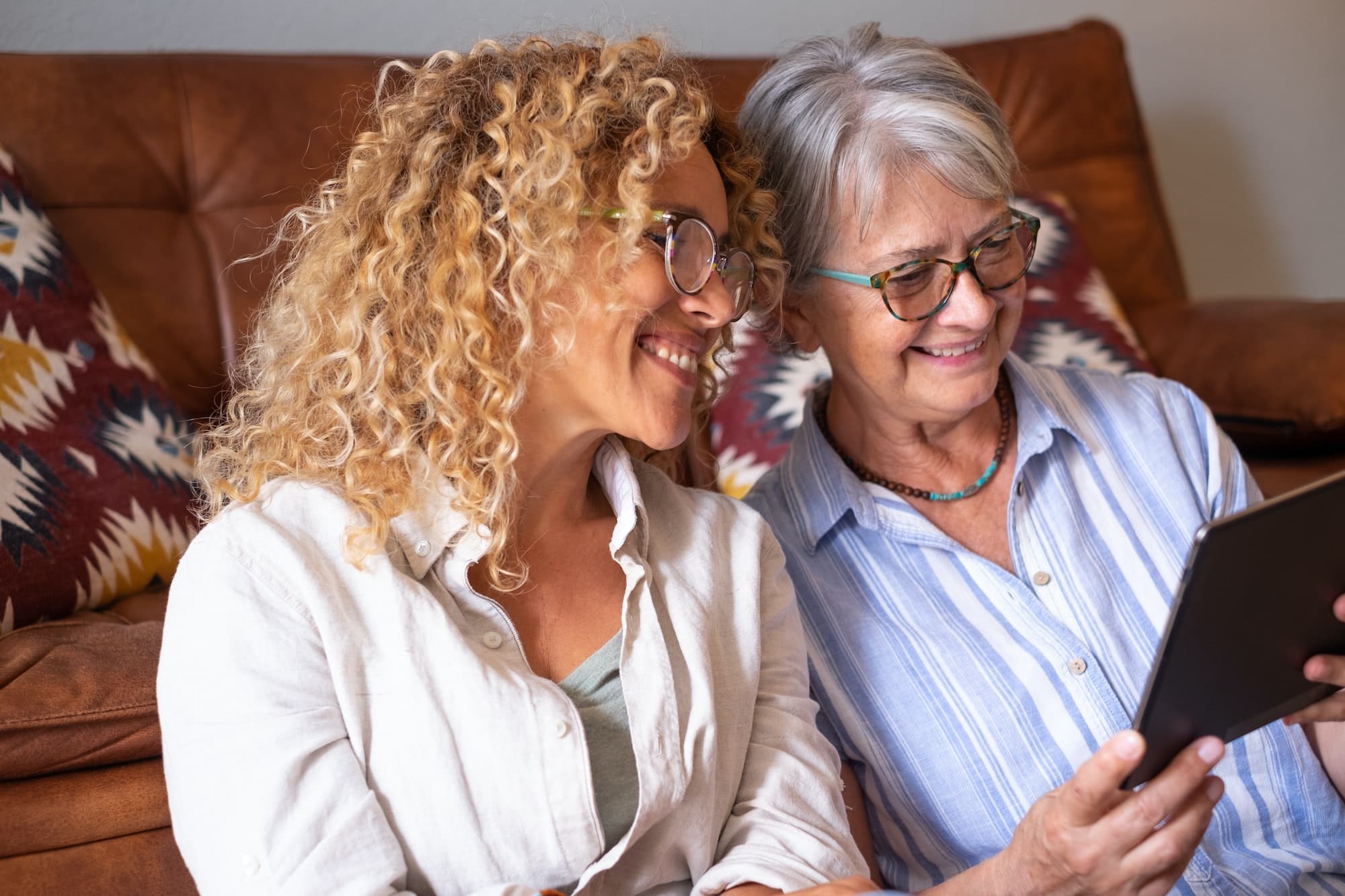 Mother with adult daughter at home having fun together sharing news on digital device